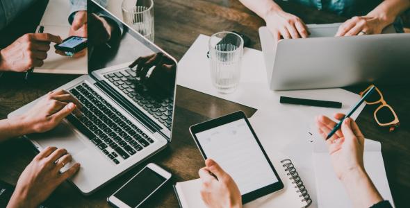 Tafel met laptops, een tablet en pen, met handen die dit vasthouden